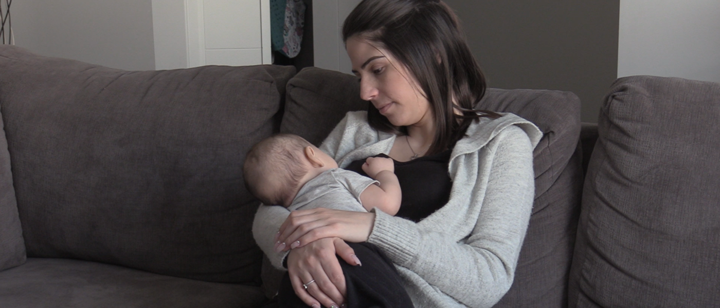 A woman sits on a couch holding a baby. She looks down at it fondly.